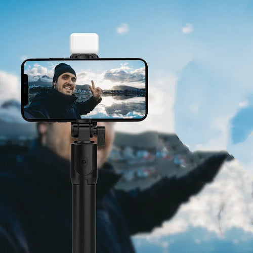 Black Bluetooth selfie stick with extended tripod legs and phone holder, shown with a smartphone attached.