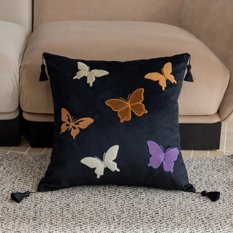 Square beige cushion with butterfly embroidery on a sofa, showing purple and black colour options.