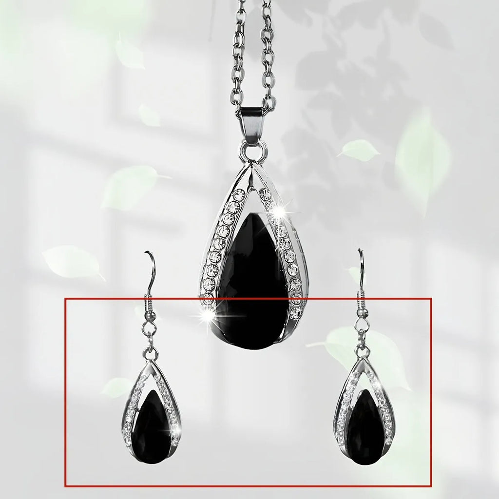 Close-up of a black alloy teardrop pendant necklace and matching drop earrings with glass details on a plain background.
