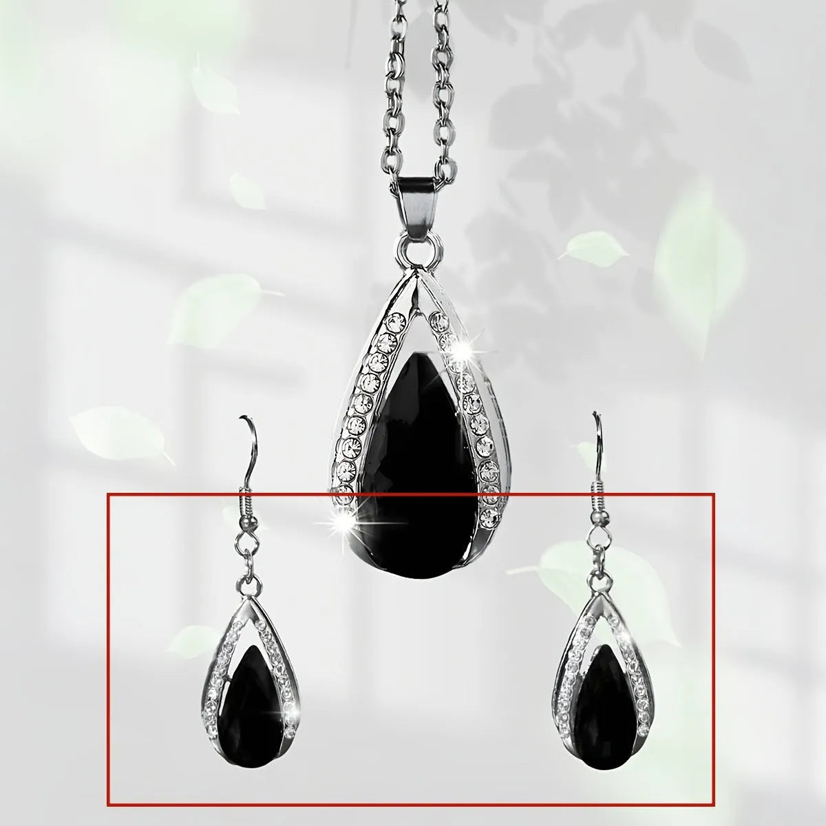Close-up of a black alloy teardrop pendant necklace and matching drop earrings with glass details on a plain background.
