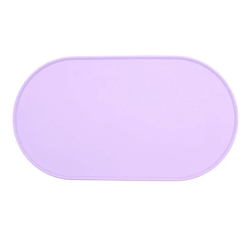 Green silicone cat feeding mat with raised edge containing a food bowl and scattered kibble on a kitchen floor.