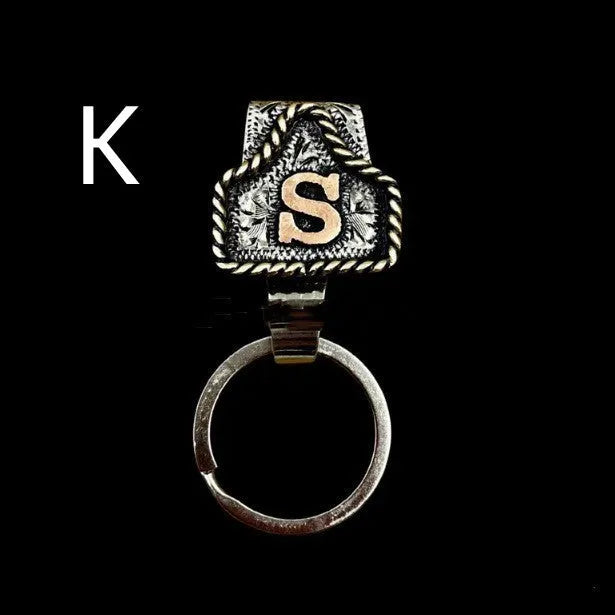 Handmade metal cow tag belt keychain showing one of 26 colour options, each marked with a different alphabet letter.