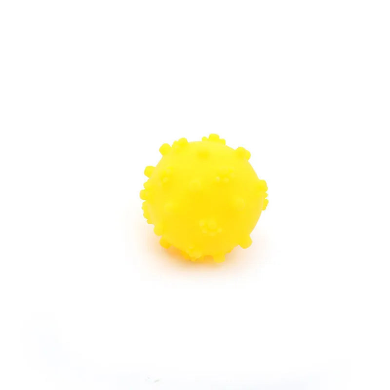 Bright blue, green, pink, and yellow spiked squeaky dog toy balls on a grass lawn.