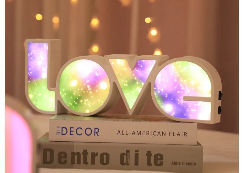 Rainbow-coloured LED LOVE decorative lamp with plastic shell on a table.