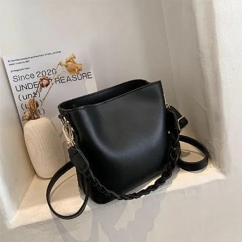 Khaki woven texture one-shoulder crossbody bucket bag with an underarm strap on a table.