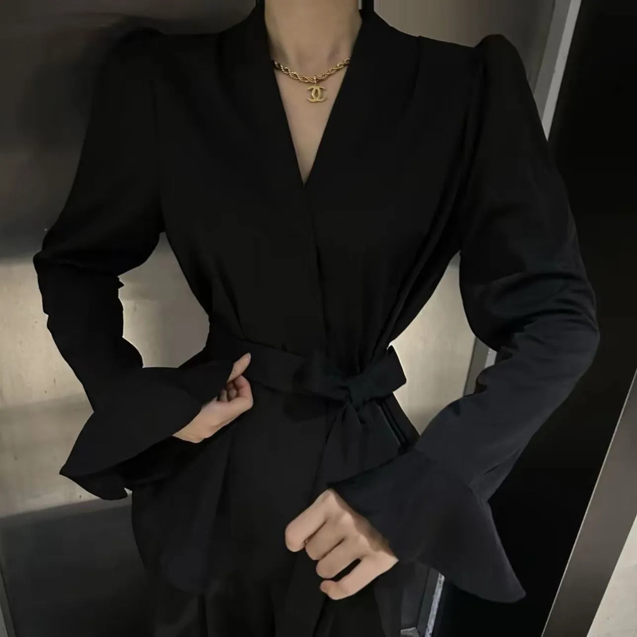 Woman wearing a black French-style shirt with an irregular collar, long bell sleeves, and a tie-front closure.