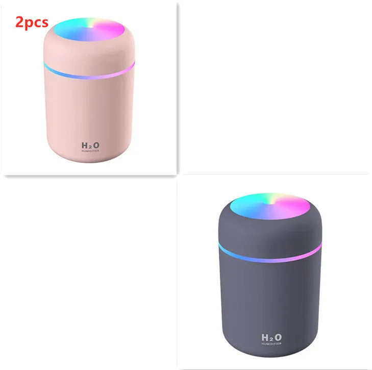Pink USB mini humidifier with LED lights on wooden desk beside laptop