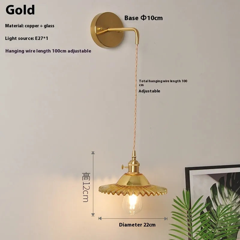 Retro brass lotus wall lamp with a smoky grey glass shade hanging on a 30cm wire beside a bed.