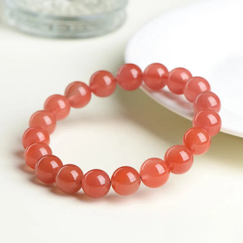 Natural cherry red agate bead bracelet with polished stones on a wrist, showing colour variation and secure clasp.