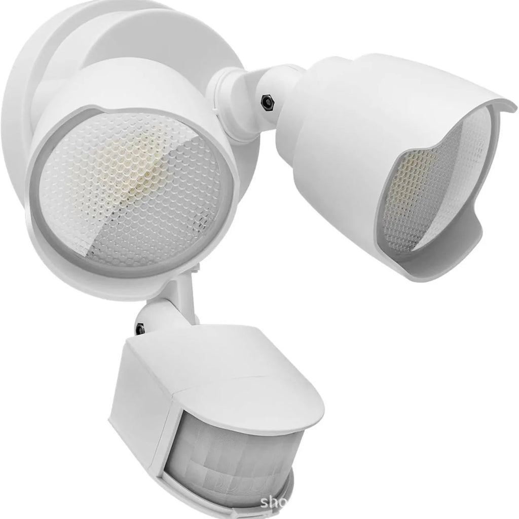 White outdoor LED security flood light with motion sensor mounted on a wall beside a garage door.