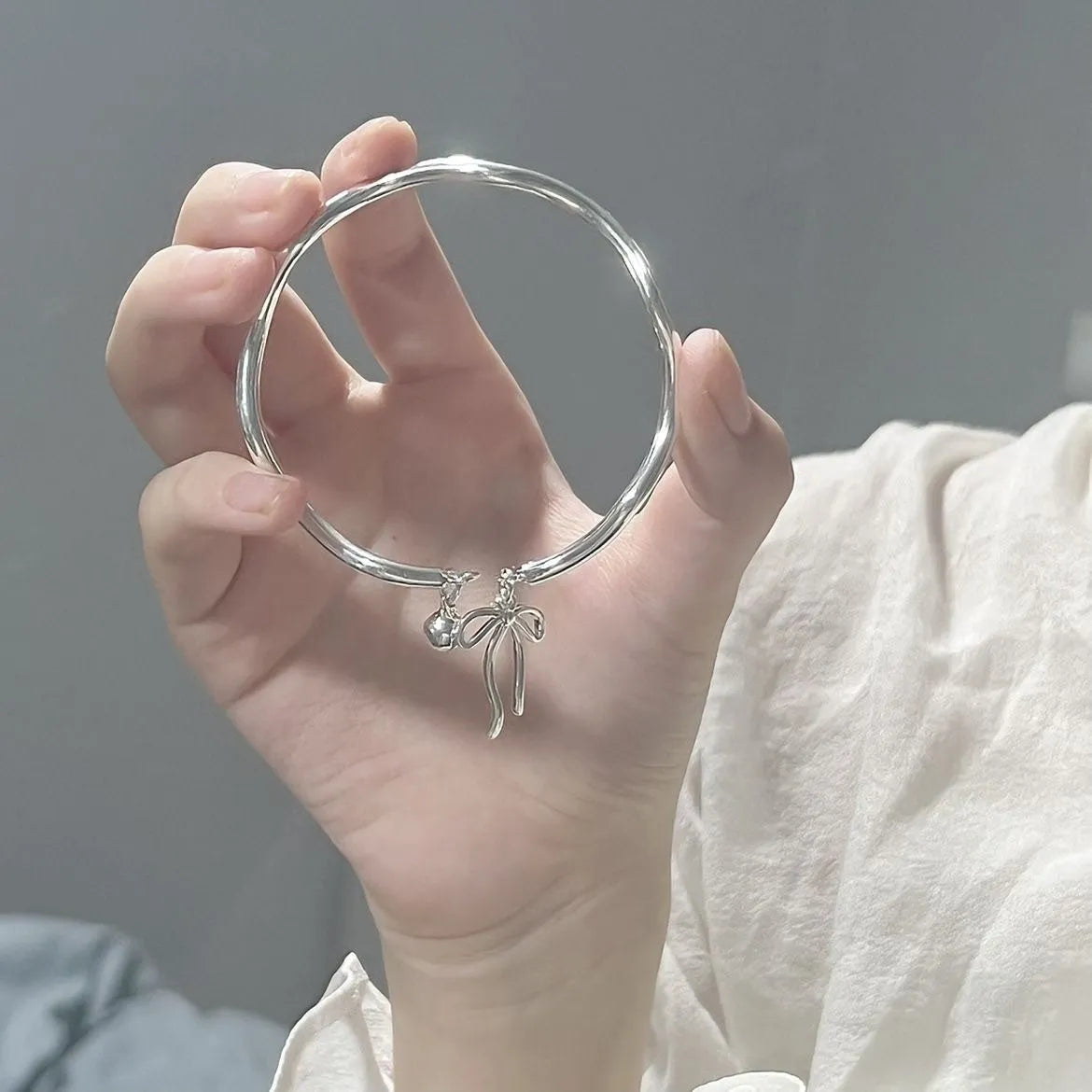 Silver tone adjustable bangle bracelet with a decorative bow charm and lobster clasp on a white background.