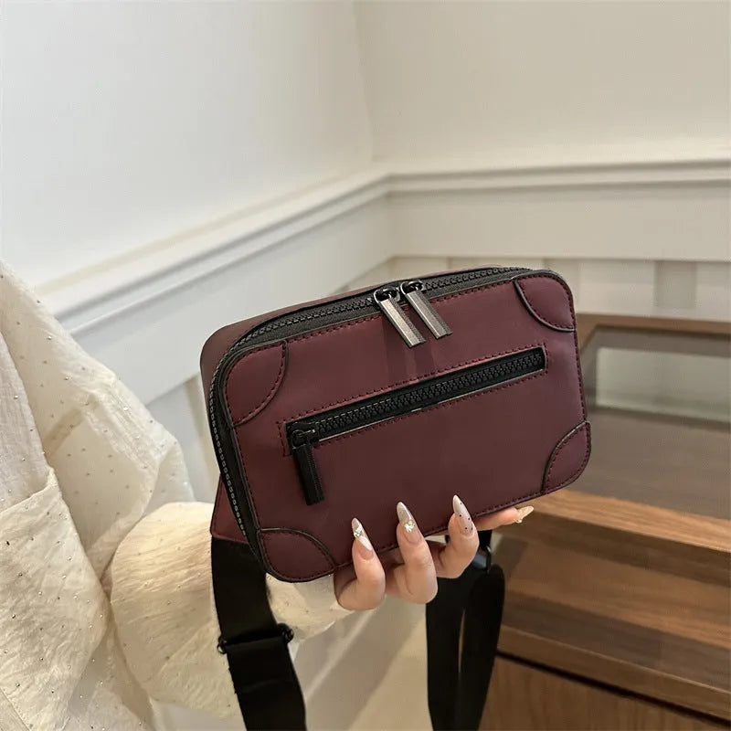 A small, square, structured crossbody bag in a choice of colours, showing its horizontal shape and sewing line detailing.