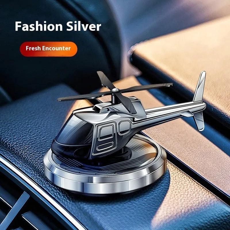 Silver metal solar-powered helicopter car air freshener rotating on a car dashboard.
