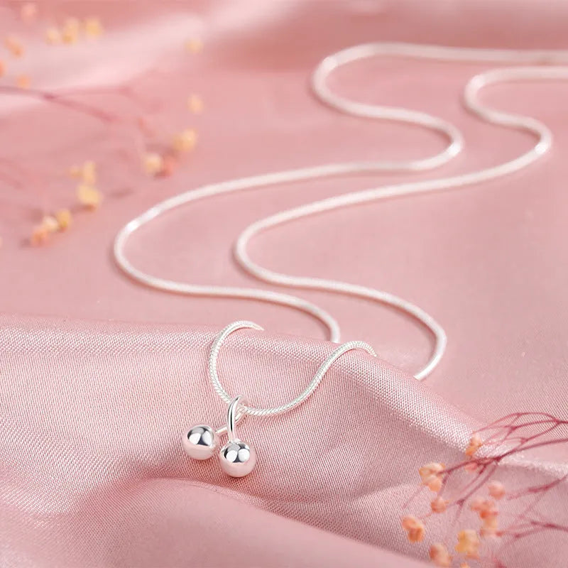 Close-up of a silver cherry pendant necklace on an adjustable snake bone chain, showing the fruit detail and spring ring clasp.