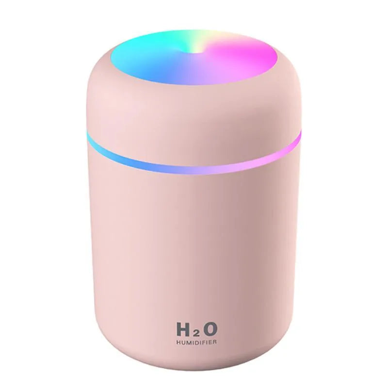 Pink USB mini humidifier with LED lights on wooden desk beside laptop