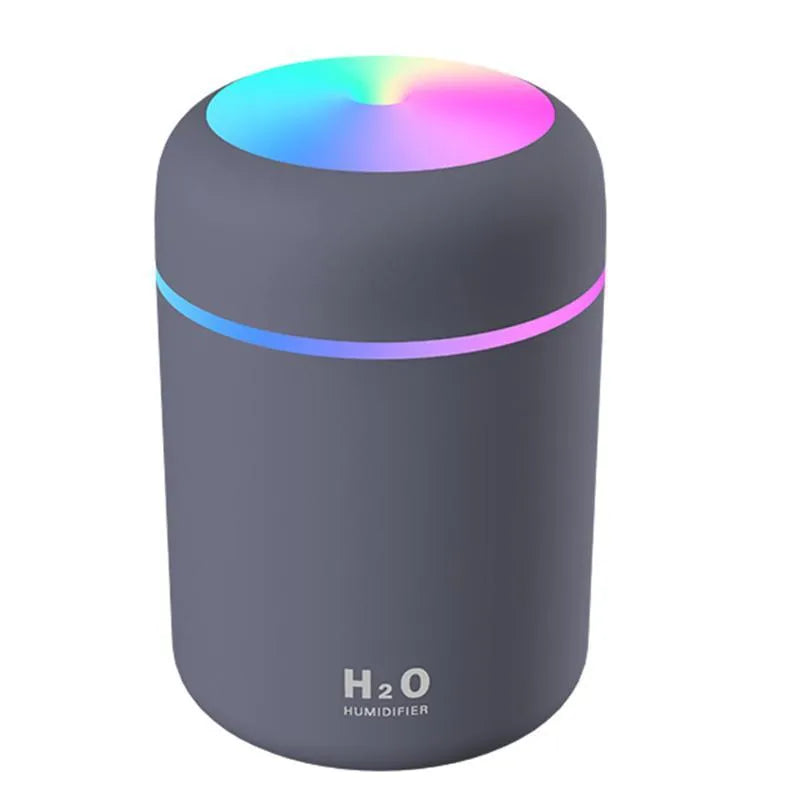 Pink USB mini humidifier with LED lights on wooden desk beside laptop