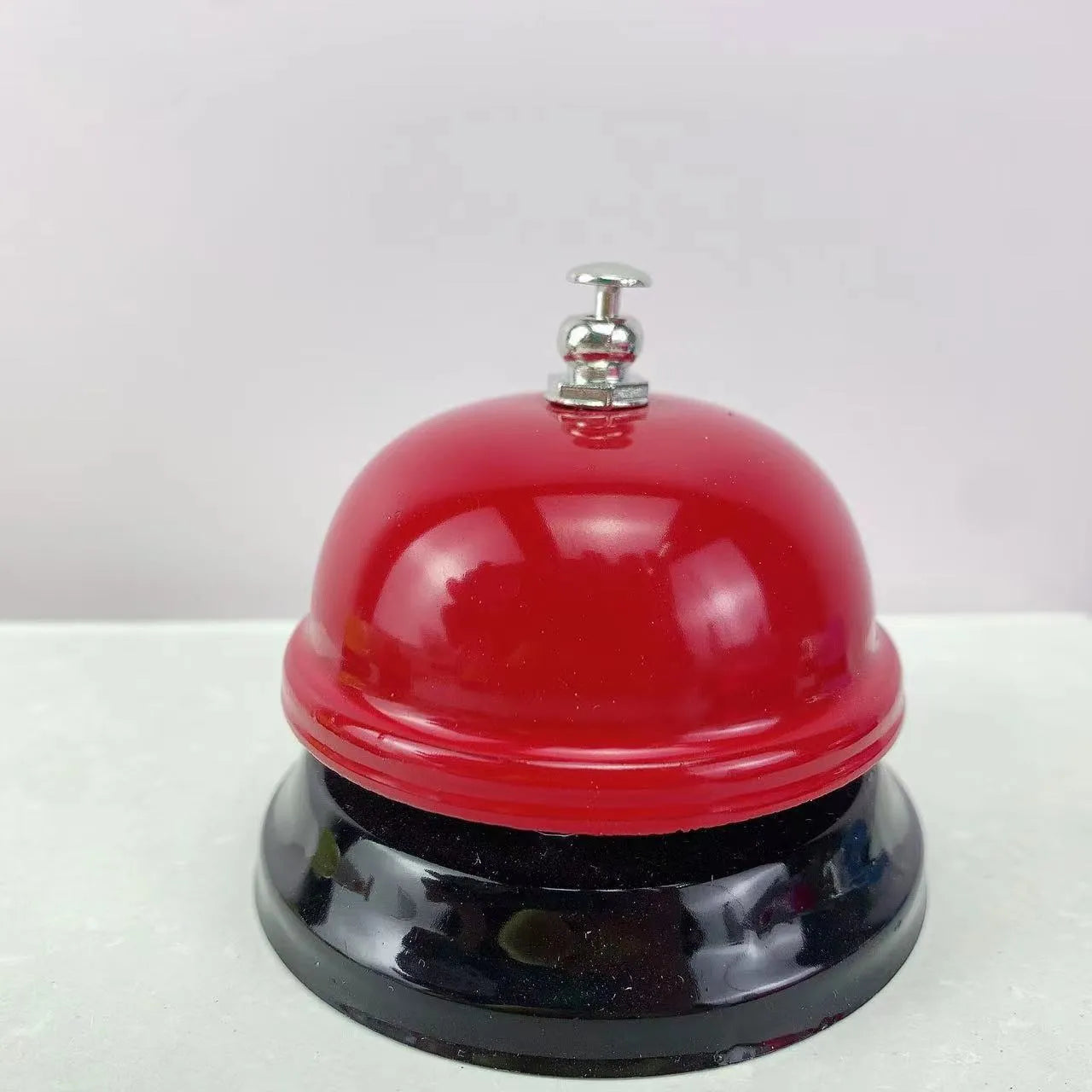 Iron table serving bell in multiple colour options on a wooden surface.