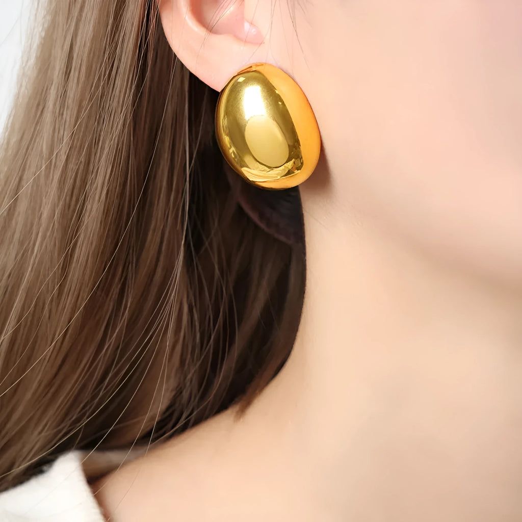 A pair of geometric gold-coloured ear studs with a glazed reflective surface and linear design details.