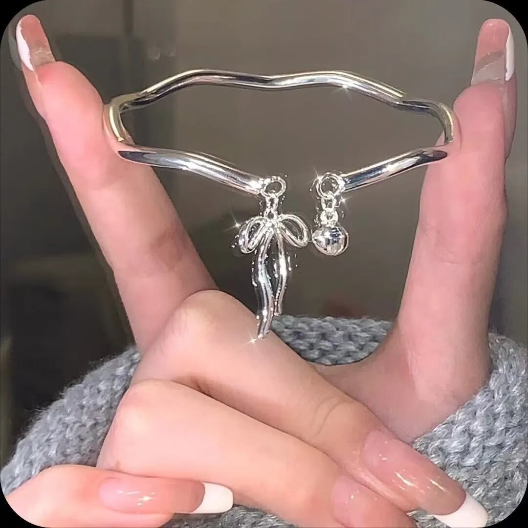 Silver tone adjustable bangle bracelet with a decorative bow charm and lobster clasp on a white background.