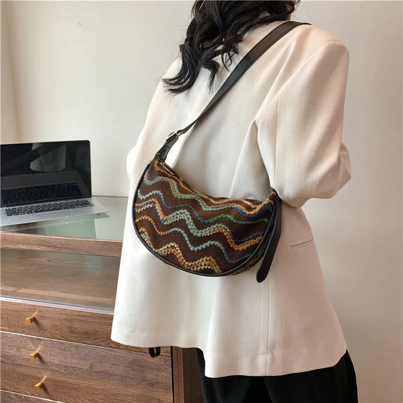 Women's straw woven crossbody bag showing knitted texture and single shoulder strap, shown in corrugated black colour.