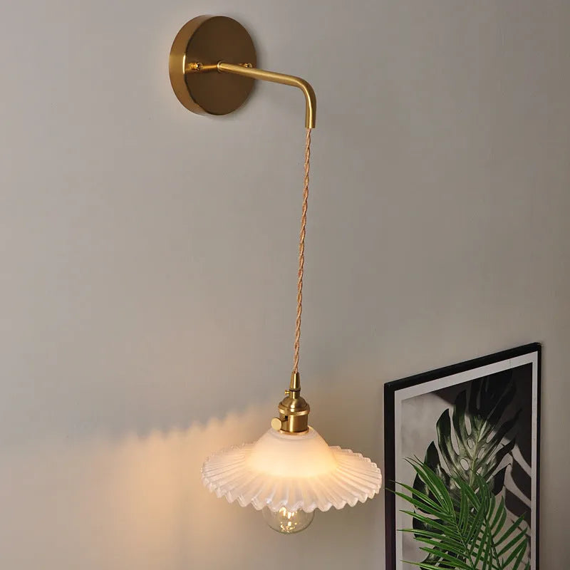 Retro brass lotus wall lamp with a smoky grey glass shade hanging on a 30cm wire beside a bed.