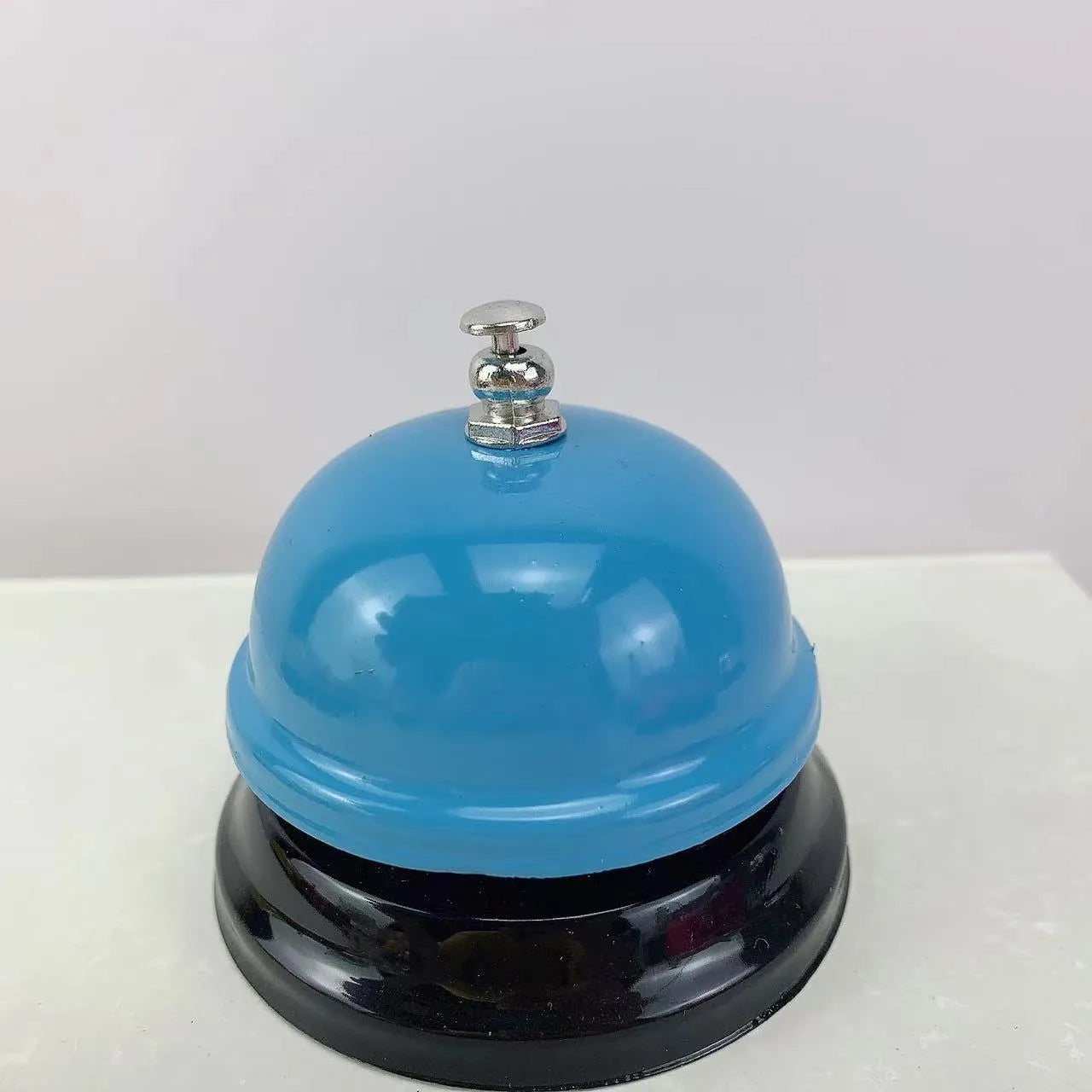 Iron table serving bell in multiple colour options on a wooden surface.