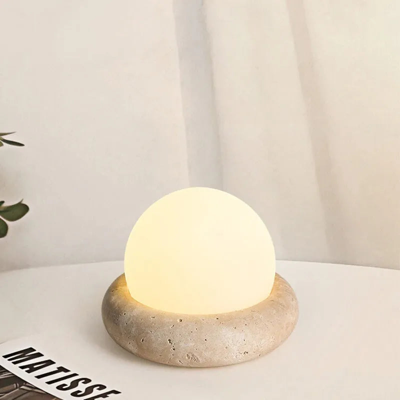 Circular modern night light with remote control on a wooden bedside table.