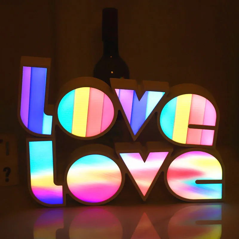 Rainbow-coloured LED LOVE decorative lamp with plastic shell on a table.