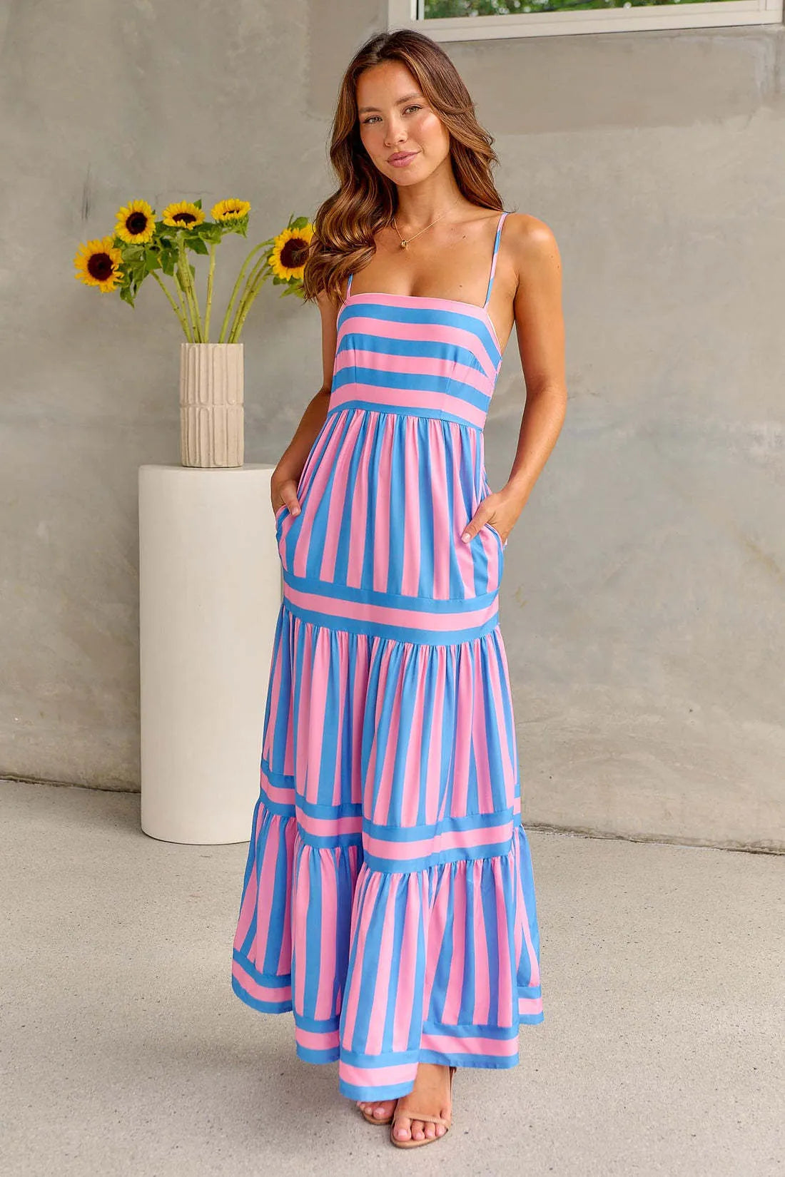 Woman wearing a striped backless suspender long dress with a square neck and side pockets.