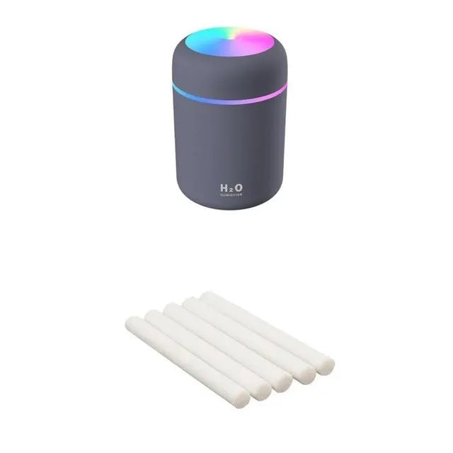 Pink USB mini humidifier with LED lights on wooden desk beside laptop