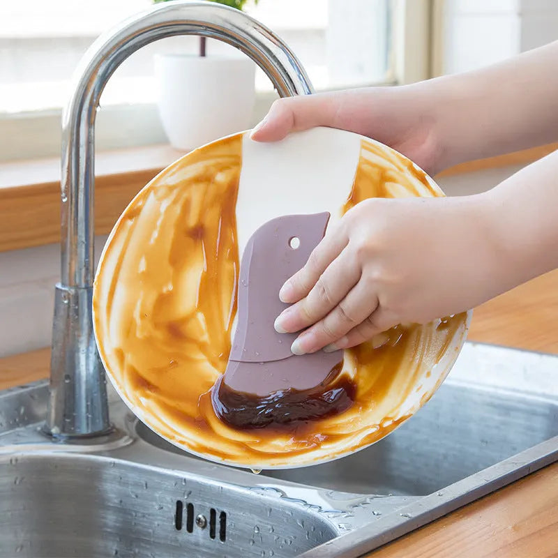 Penguin-shaped soft blade kitchen scraper tool for cleaning plates and pans in green, grey, or pink colours