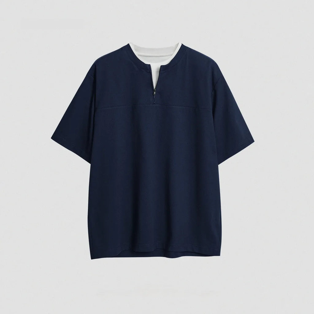 A solid colour loose-fitting casual top with zip detail and patchwork styling on a hanger.