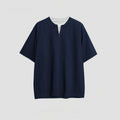 A solid colour loose-fitting casual top with zip detail and patchwork styling on a hanger.