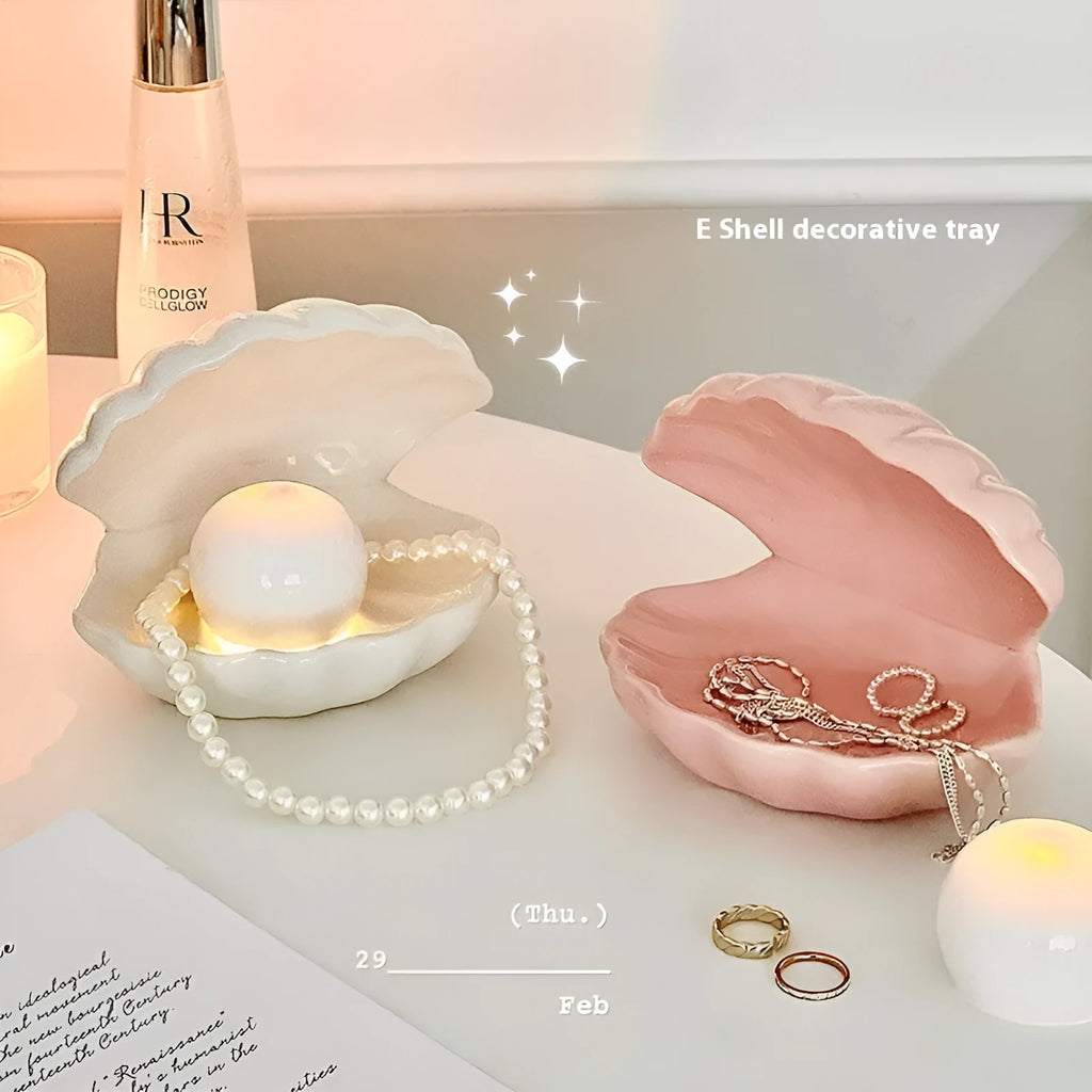 White porcelain scallop shell tray with optional warm LED night light, holding small jewellery on a bedside table.