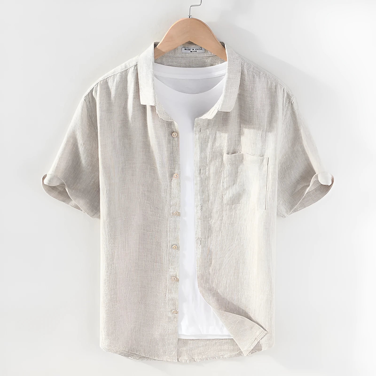 Men's raw jute coloured linen shirt with a square collar and short sleeves on a hanger.