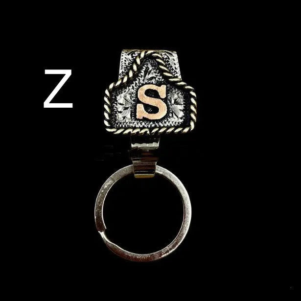 Handmade metal cow tag belt keychain showing one of 26 colour options, each marked with a different alphabet letter.