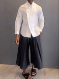 White asymmetrical shirt and black pleated trousers co-ordinate set laid flat