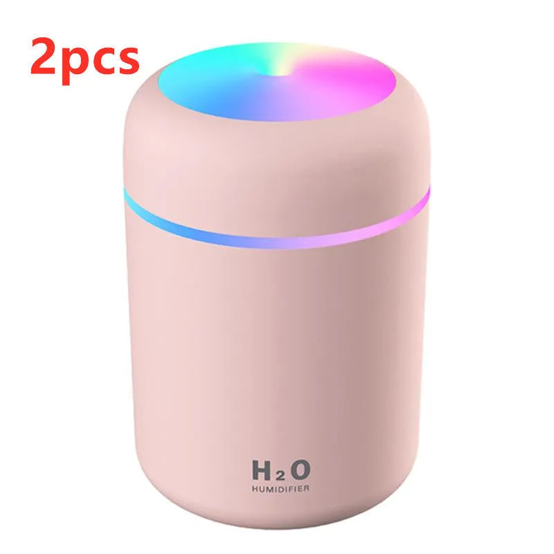 Pink USB mini humidifier with LED lights on wooden desk beside laptop