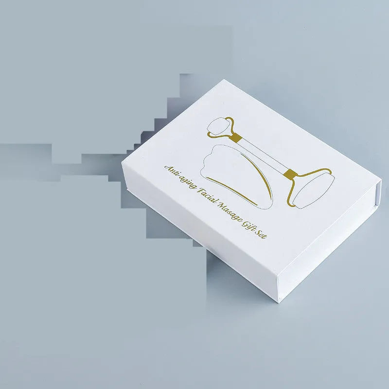 Natural white jade facial roller and gua sha scraper board set on a plain background.