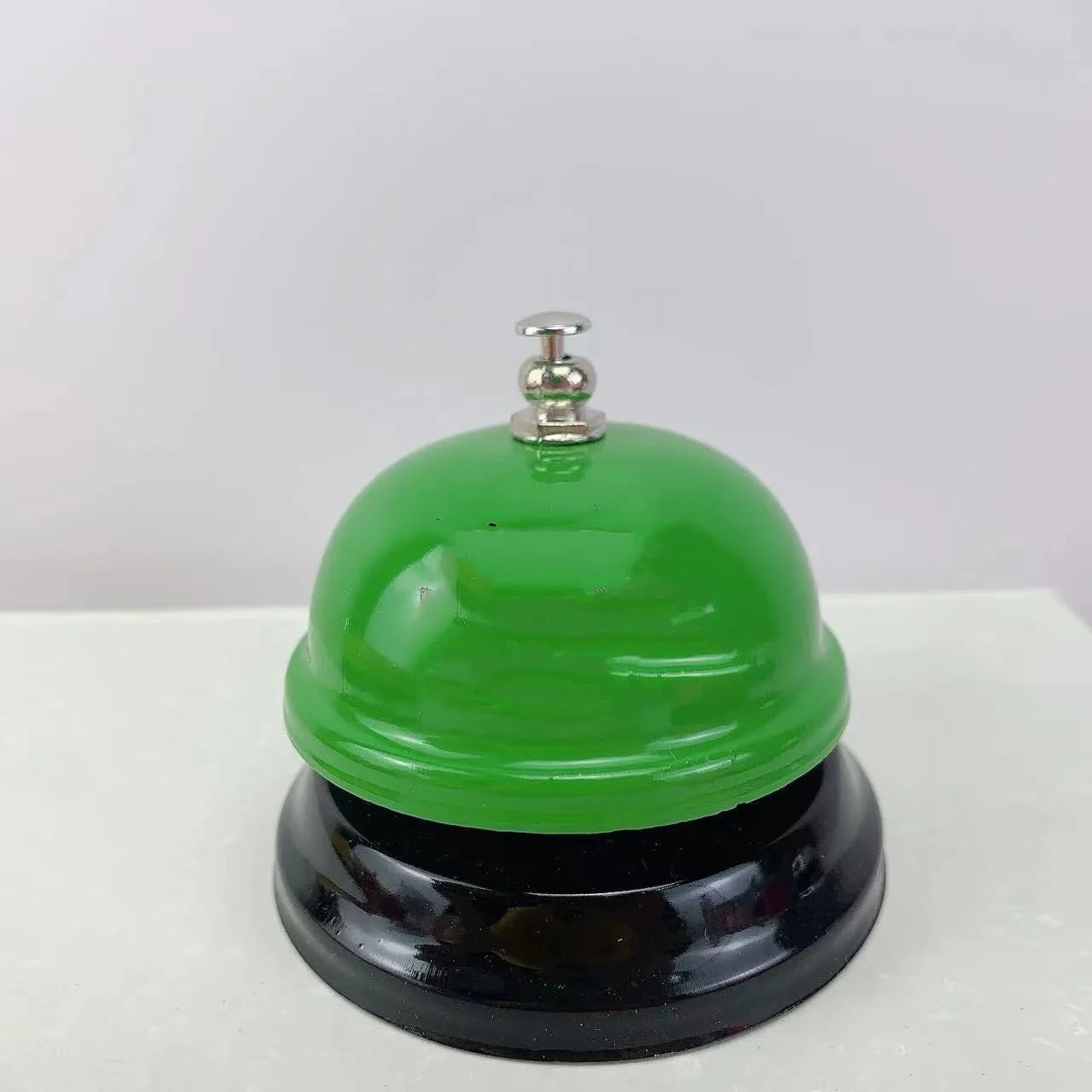 Iron table serving bell in multiple colour options on a wooden surface.