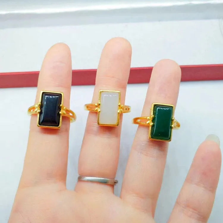 Adjustable brass gold-plated ring with a green artificial gemstone inlay on a finger.