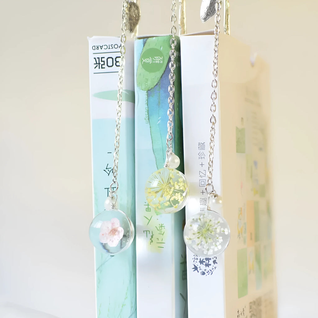 Close-up of a metal alloy bookmark with real dried pink flowers sealed inside, on an open book.