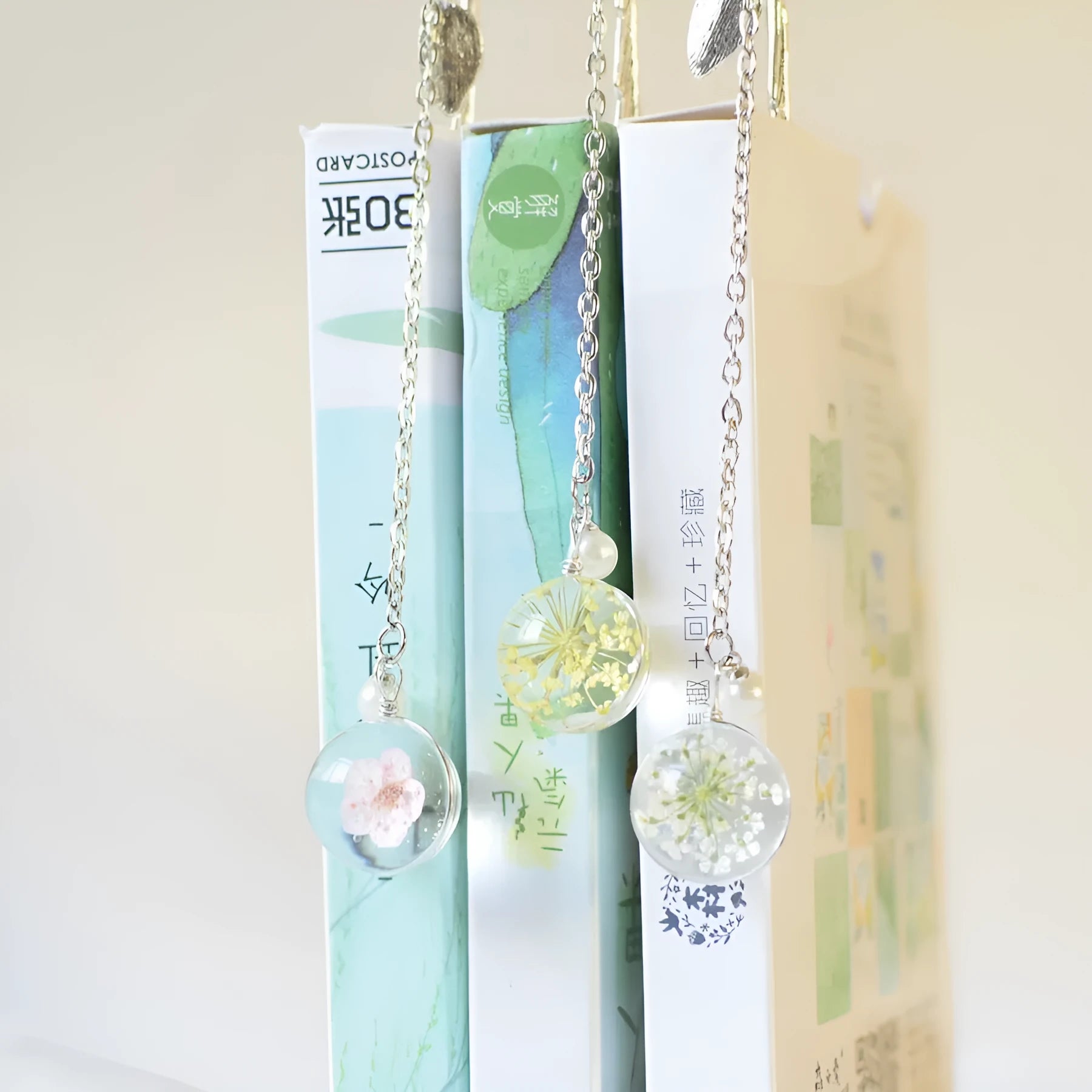 Close-up of a metal alloy bookmark with real dried pink flowers sealed inside, on an open book.