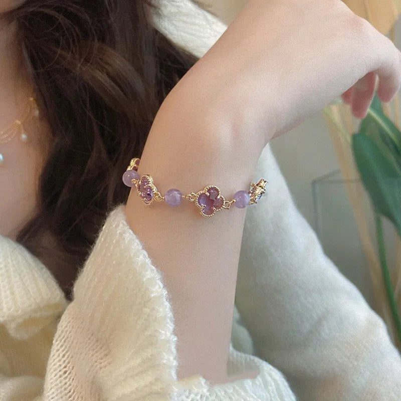 Women's artificial amethyst bracelet with four-leaf clover charm and pearl accents on a wrist.