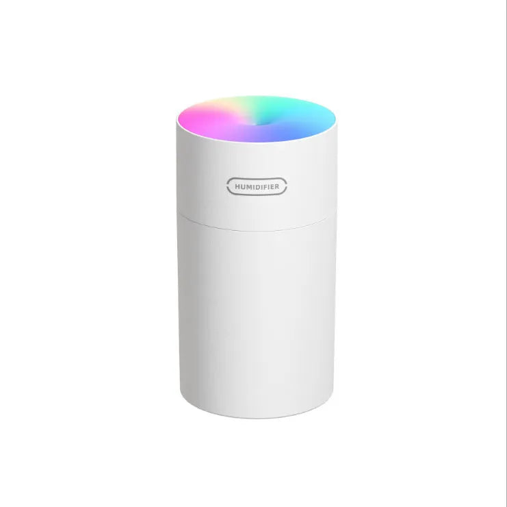 Pink USB mini humidifier with LED lights on wooden desk beside laptop