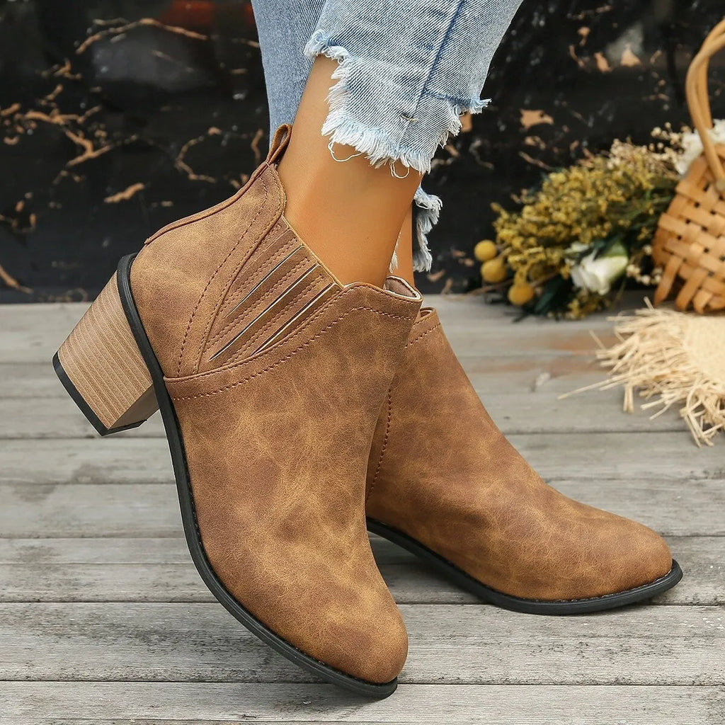 Women's black slip-on ankle boots with pointed toe and thick square heel on a wooden floor.