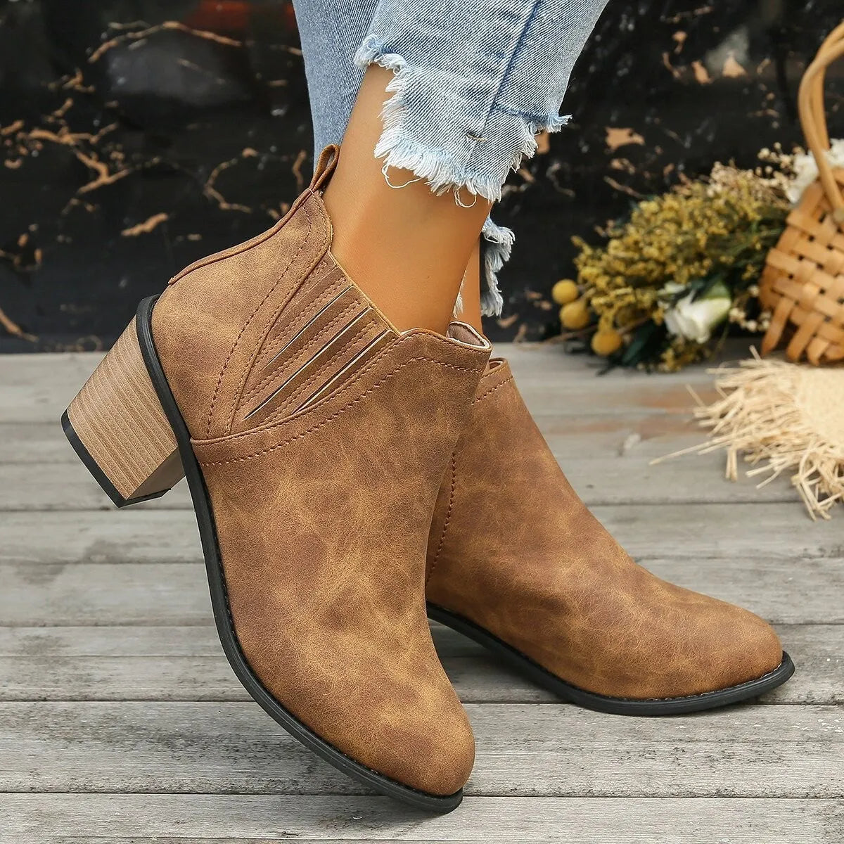 Women's black slip-on ankle boots with pointed toe and thick square heel on a wooden floor.