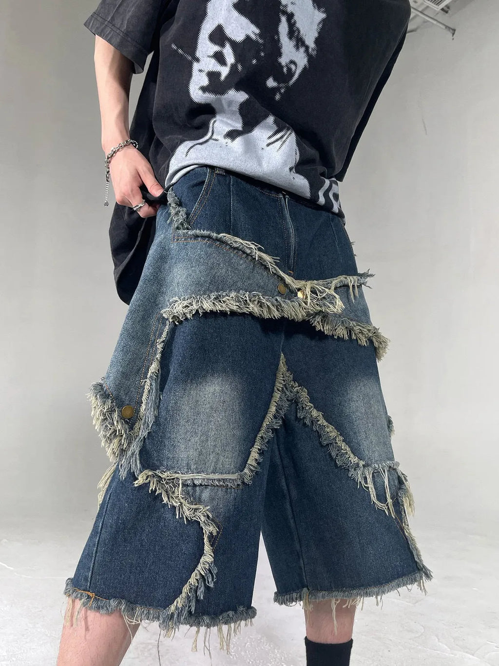 Man wearing blue loose-fit denim shorts with frayed five-pointed star embroidery on the leg.