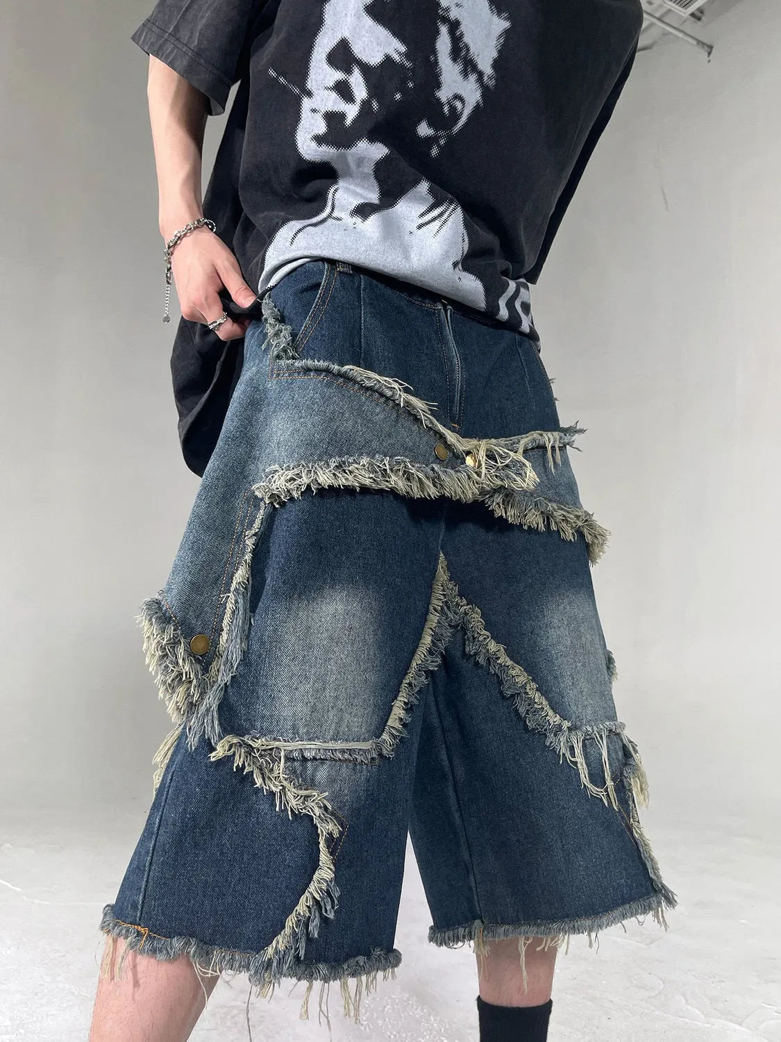 Man wearing blue loose-fit denim shorts with frayed five-pointed star embroidery on the leg.