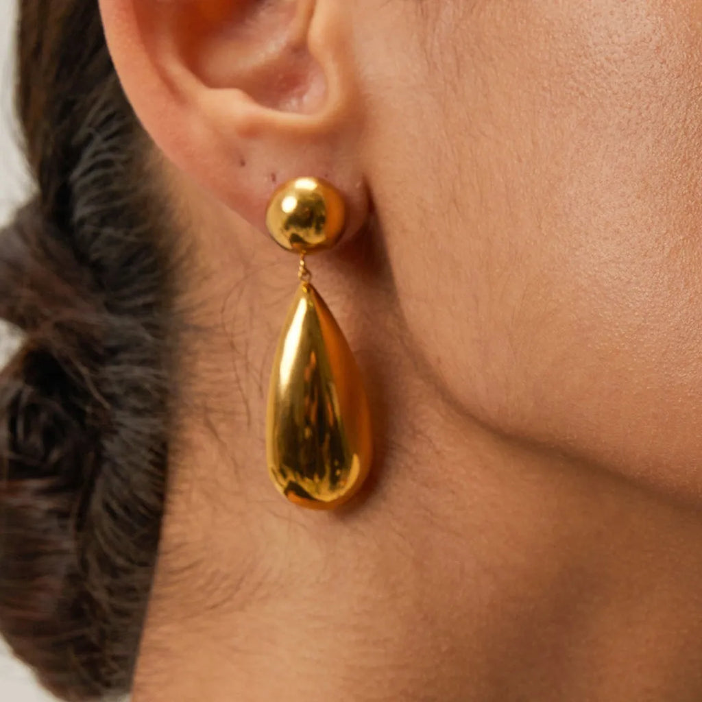 A pair of gold geometric hemisphere earrings with a water droplet pendant design on a white background.
